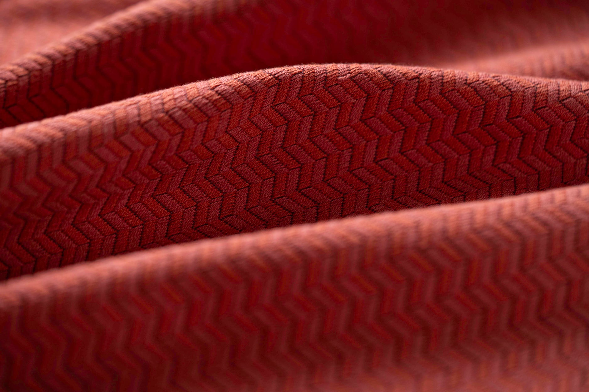 Close-up of red textured fabric with a herringbone pattern light folded. 