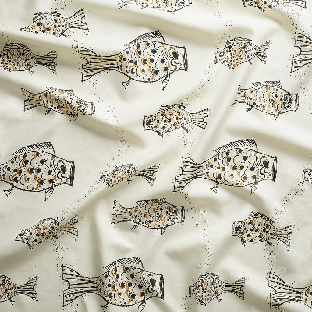 Close up of gently draped printed linen with a pattern of hand-drawn fish in black with tan and brown scales and scattered bubble dots on white. 