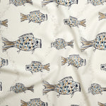 Close up of gently draped printed linen with a pattern of hand-drawn fish in navy with tan and blue scales and scattered bubble dots on white. 