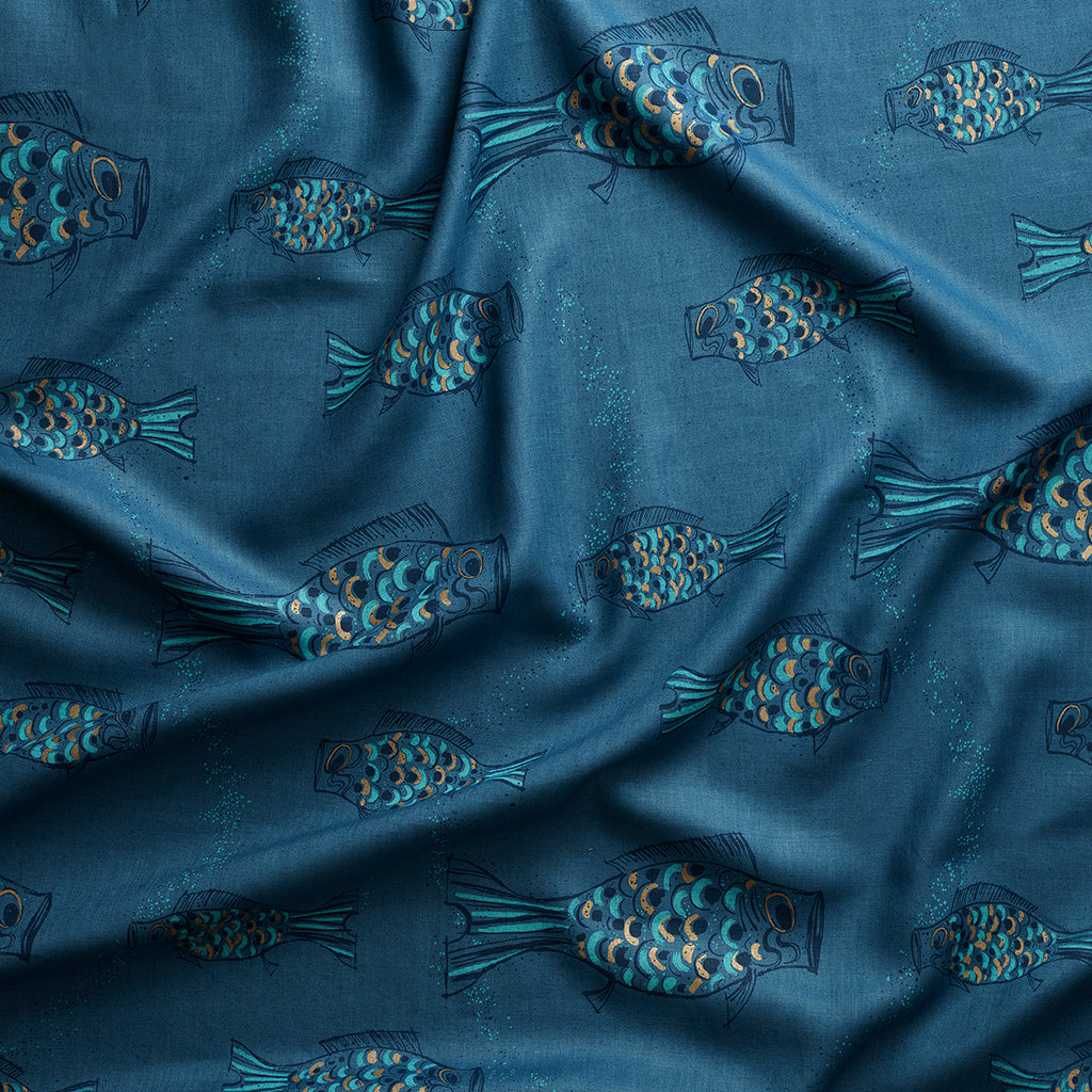 Close up of gently draped printed linen with a pattern of hand-drawn fish in navy with tan and  blue scales and scattered bubble dots on dark blue.