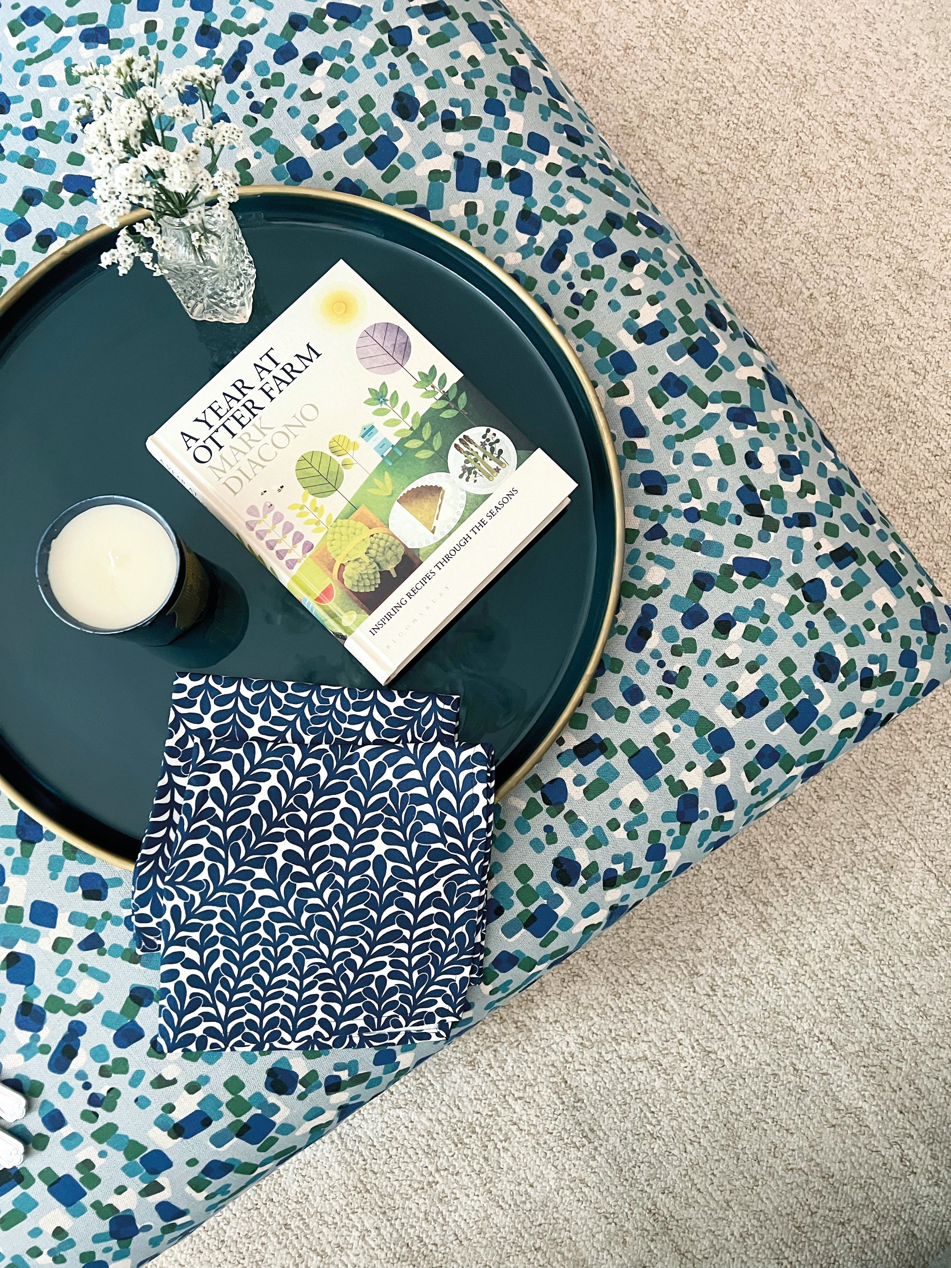 A fabric ottoman upholstered in a playful polka dot print and topped with a tray, candle and book.