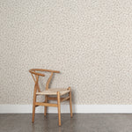Angled wooden chair with woven seat on concrete floor against wallpaper in a painterly animal print in shades of beige, grey and cream. 