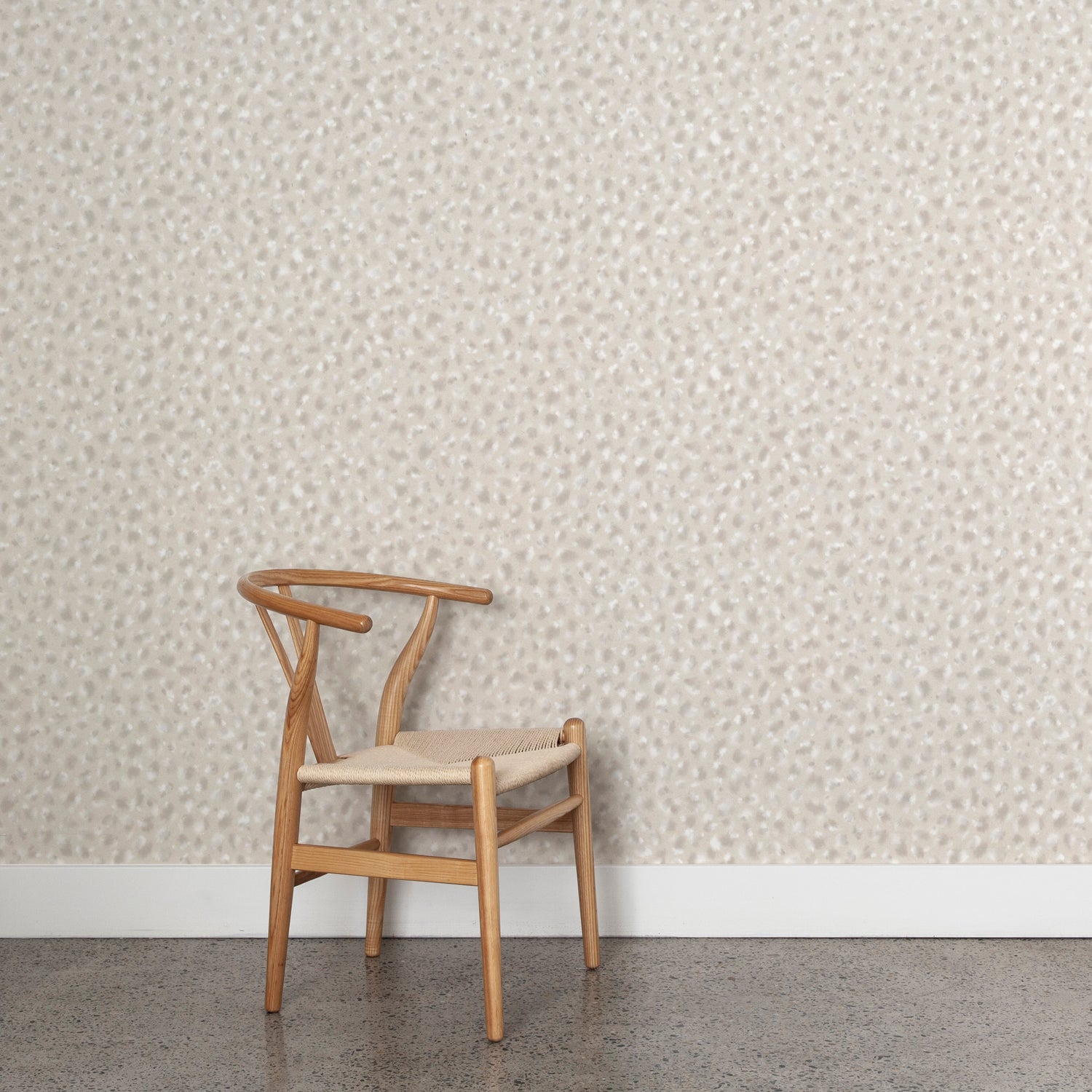 Angled wooden chair with woven seat on concrete floor against wallpaper in a painterly animal print in shades of beige, grey and cream. 