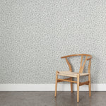 Angled wooden chair with woven seat on concrete floor against wallpaper in a painterly animal print in shades of cool blue and white. 