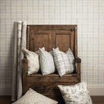 Wooden bench with patterned cushions against a plaid wallpapered wall.