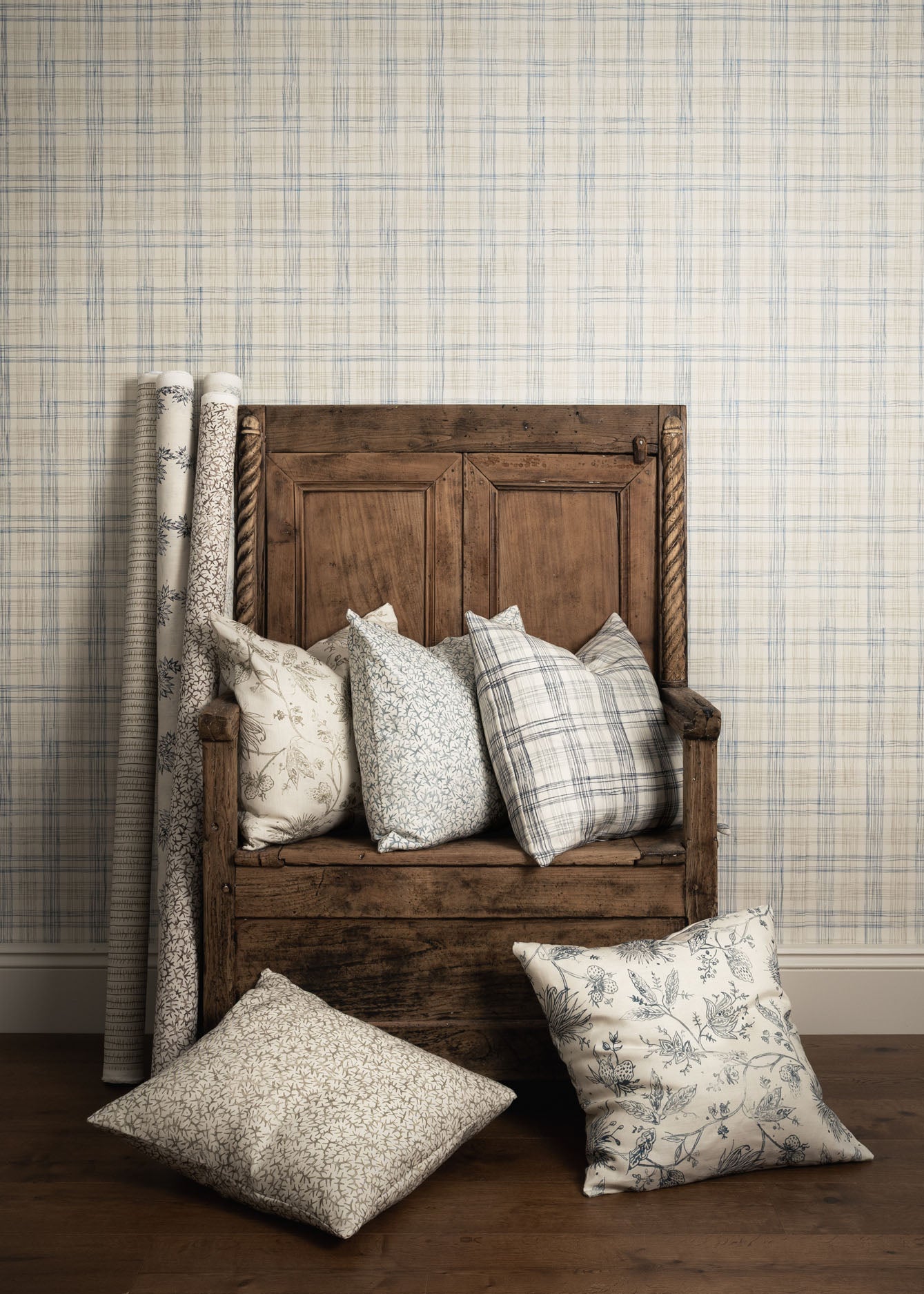 Wooden bench with patterned cushions against a plaid wallpapered wall.