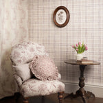 Decorative armchair with floral pattern in a room with patterned wallpaper and a small table with flowers.