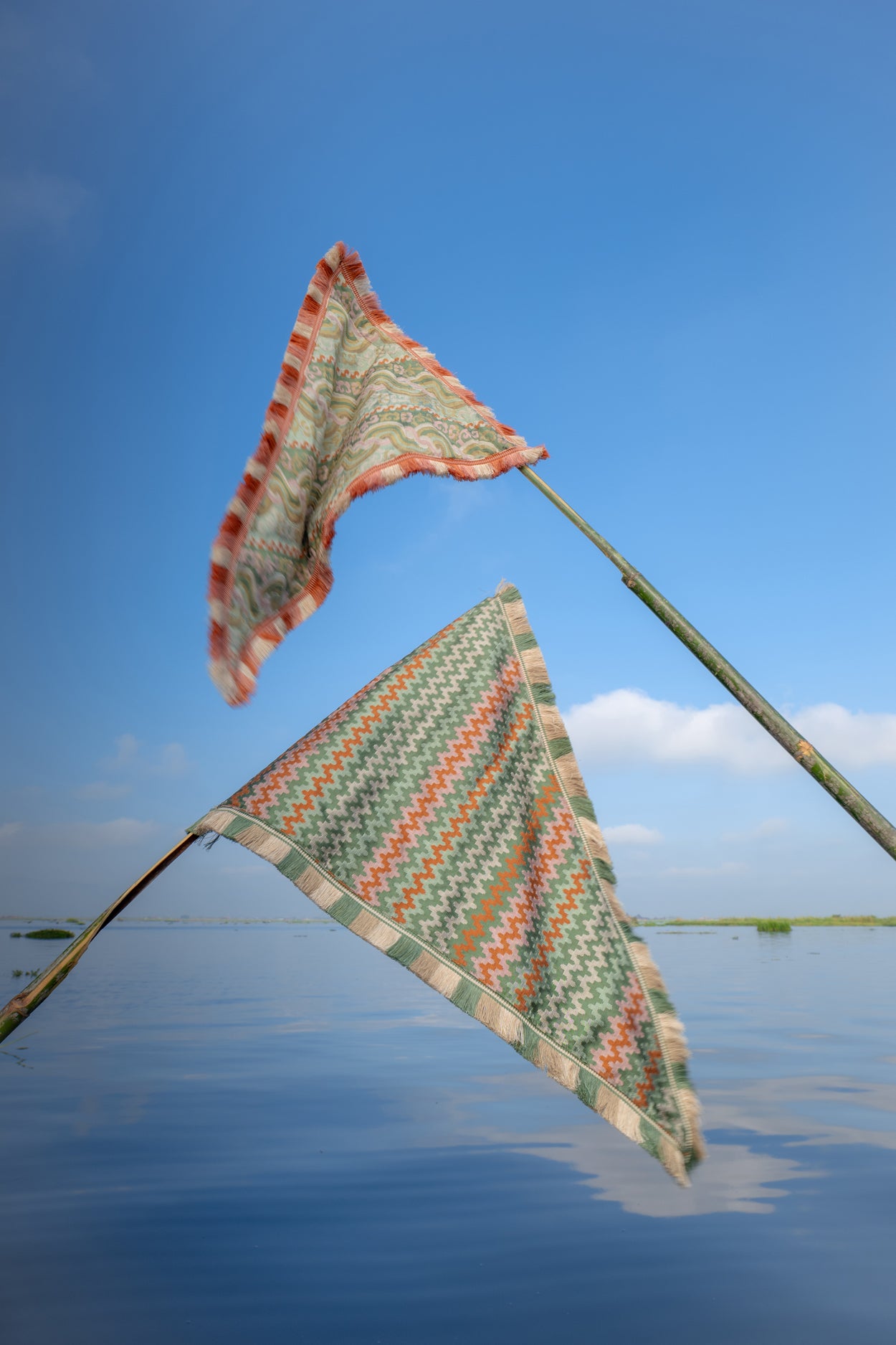 Two colorful triangular flags on a stick over a body of water with a clear blue sky.