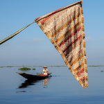 Traditional boat with a colorful flag in the foreground on a calm body of water under a clear blue sky.