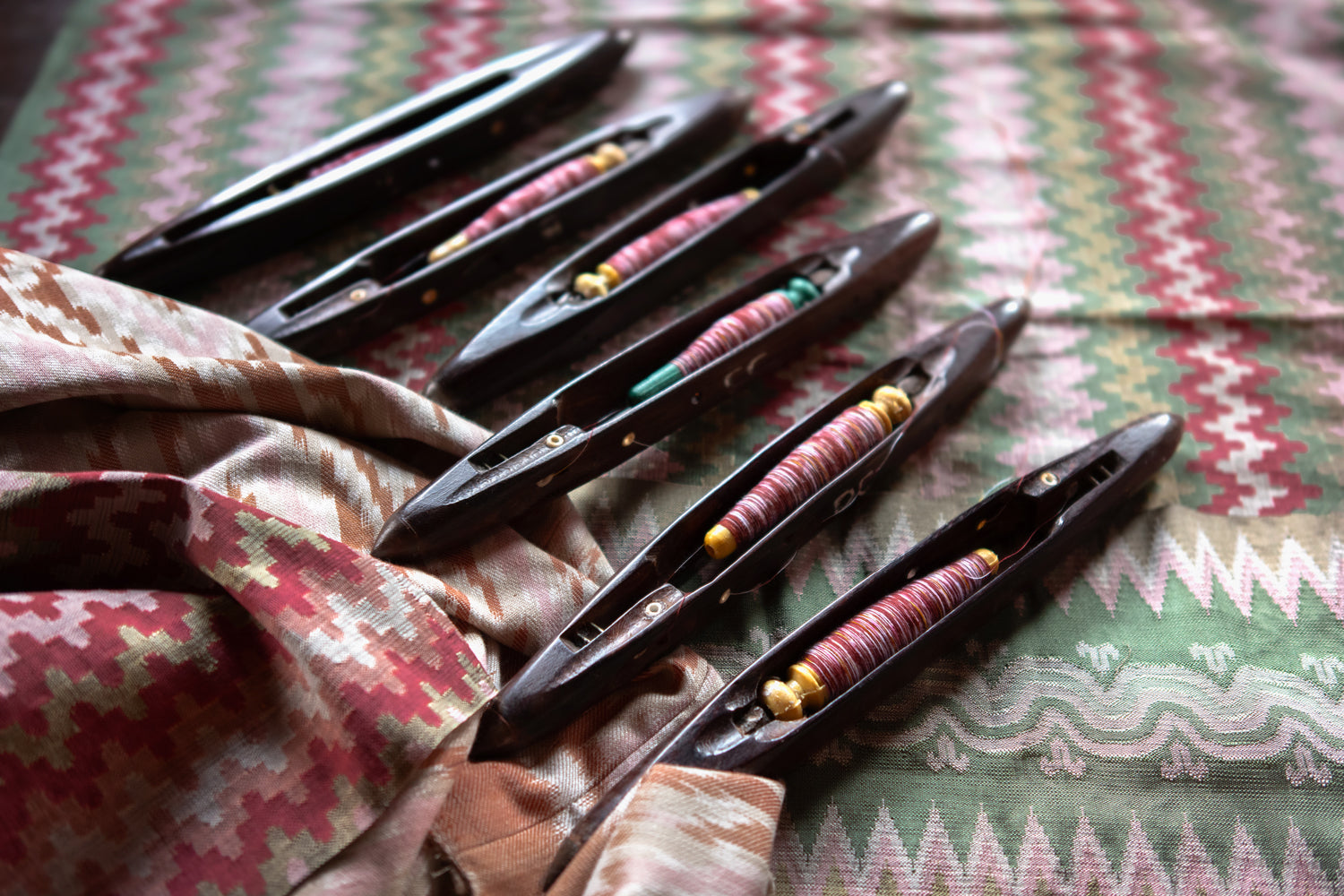 Set of black weaving shuttles with colorful thread on a patterned fabric background