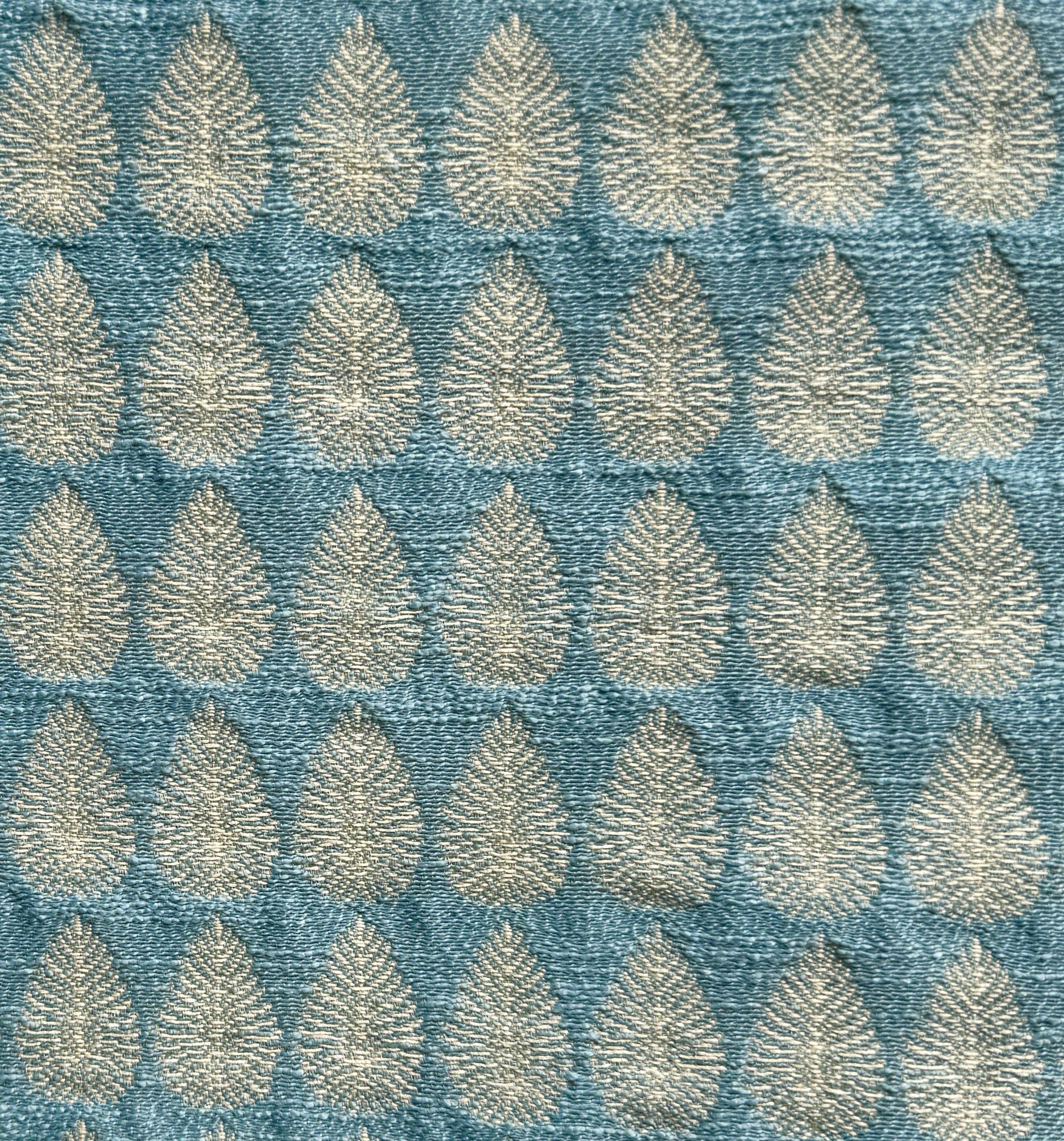 Detail of fabric woven in a repeating leaf print in shades of blue and gold.