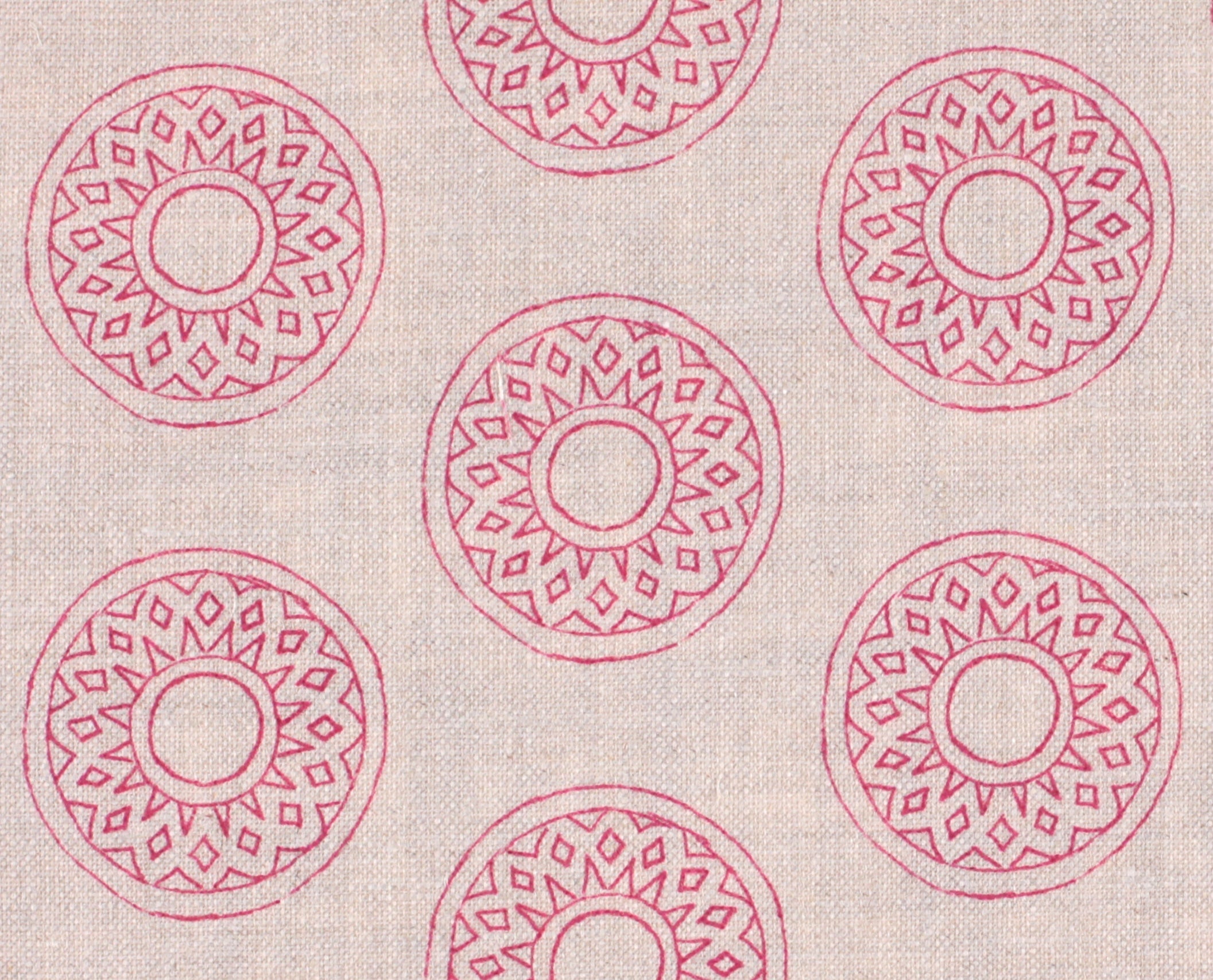 Detail of fabric in a repeating circular geometric print in pink on a cream field.