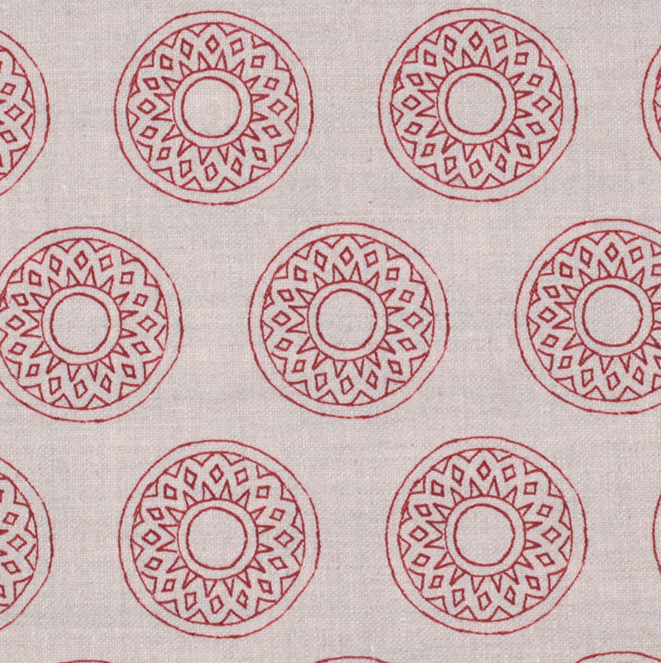 Detail of fabric in a repeating circular geometric print in red on a greige field.