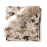 Stacked swatches of fabric in a painterly leaf print in shades of warm brown on a white background.