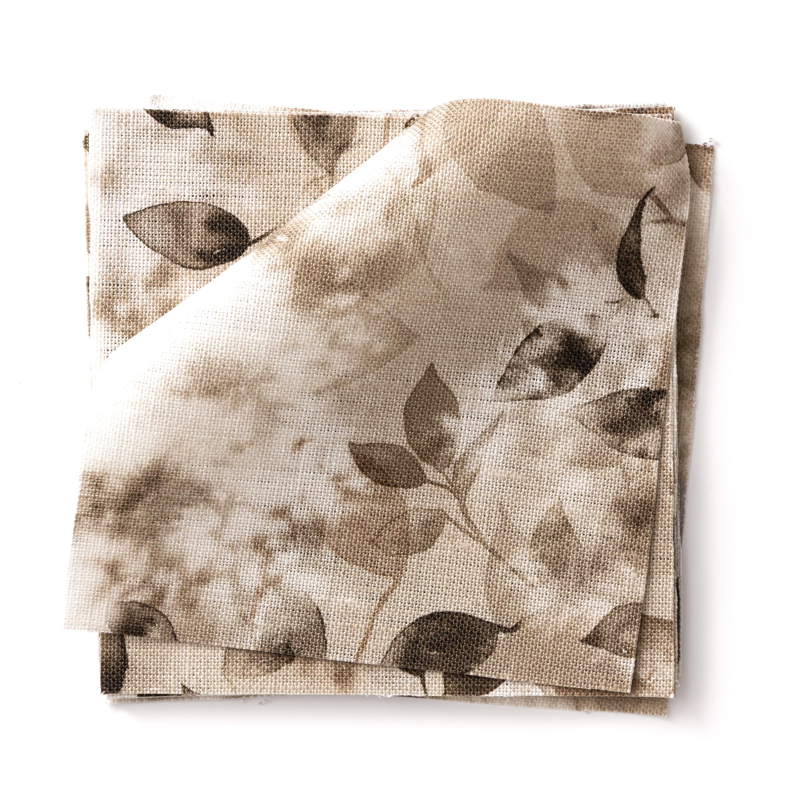 Stacked swatches of fabric in a painterly leaf print in shades of warm brown on a white background.