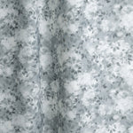 Gently draped fabric in a painterly leaf print in shades of steel blue and teal with a mottled white overlay.