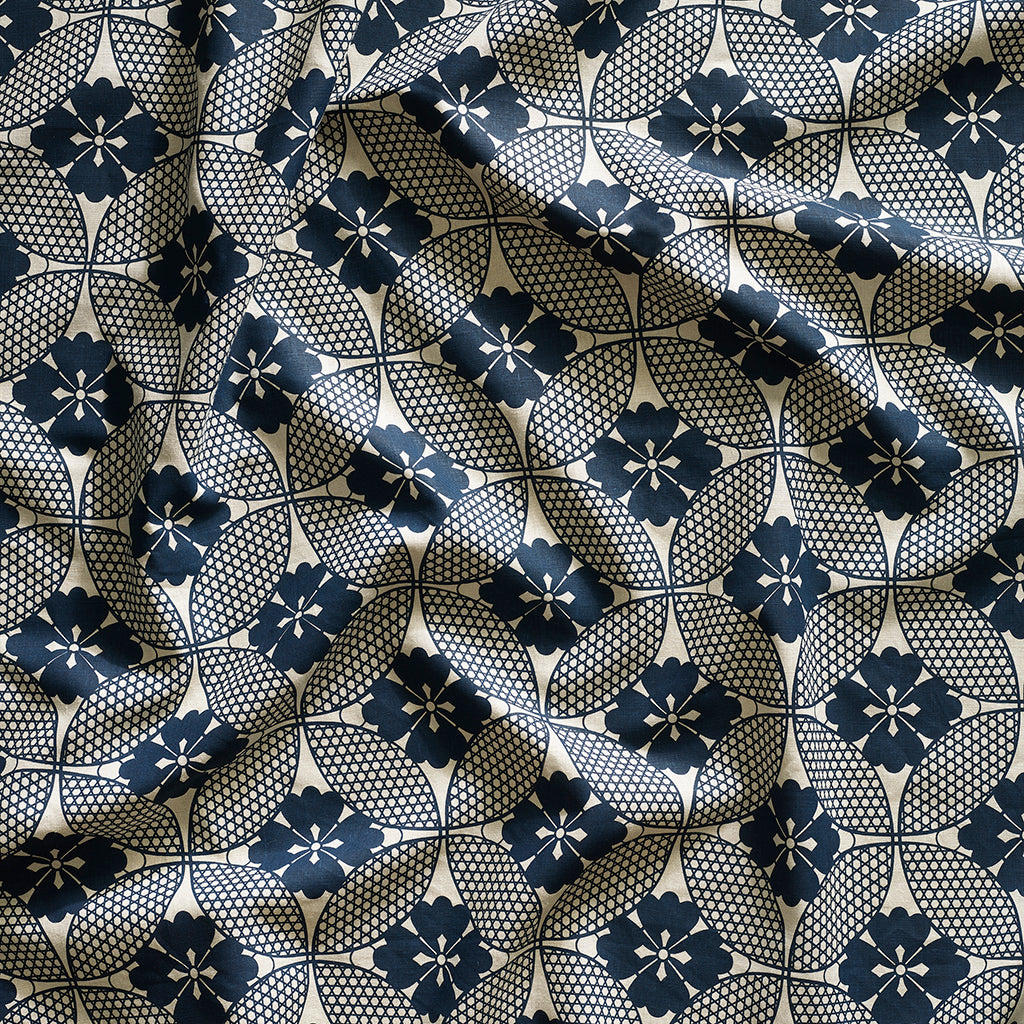 A close-up of gently draped printed linen featuring a Japanese inspired floral lattice design in navy blue on white. 