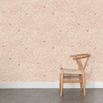 A wooden chair stands in front of a wall papered in a playful bird and leaf print in pink on a cream field.