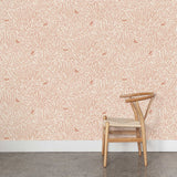 A wooden chair stands in front of a wall papered in a playful bird and leaf print in pink on a cream field.