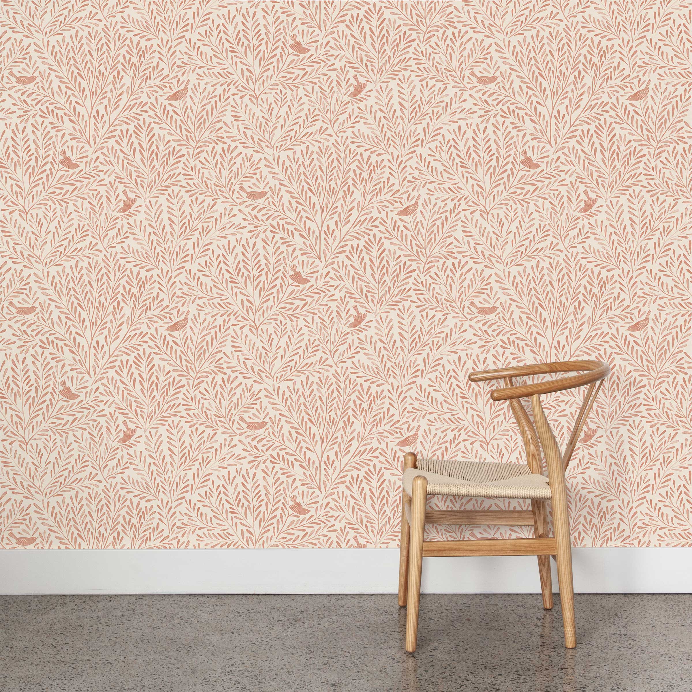 A wooden chair stands in front of a wall papered in a playful bird and leaf print in pink on a cream field.