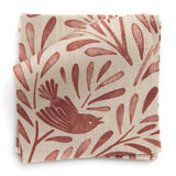 A stack of fabric swatches in a playful bird and leaf print in red on a cream field.