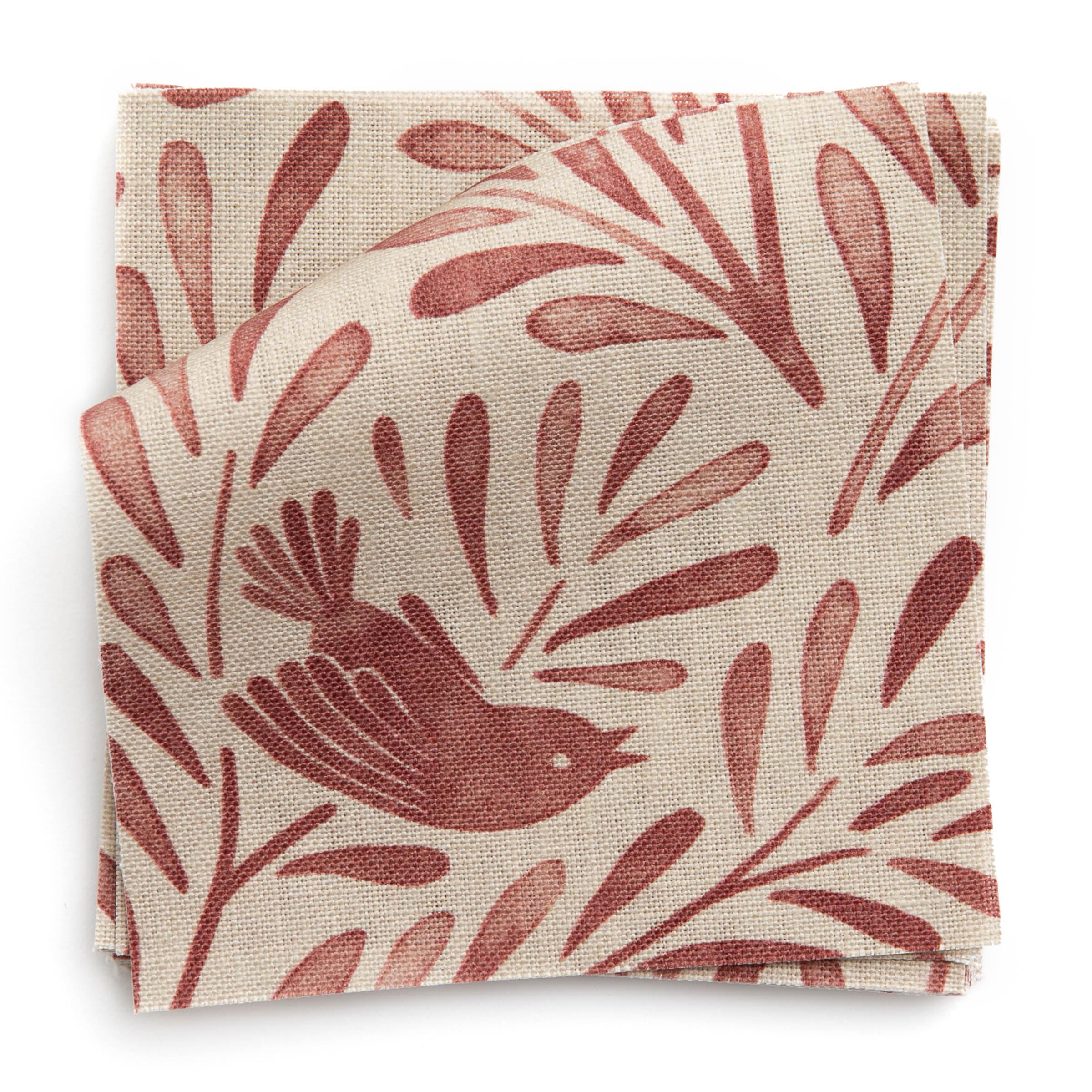 A stack of fabric swatches in a playful bird and leaf print in red on a cream field.