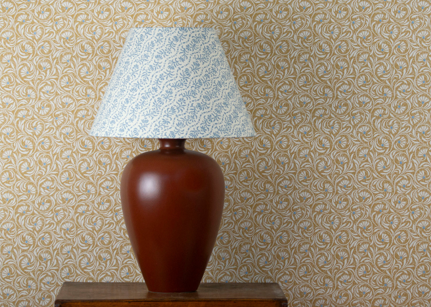 Table with decorative lamp against wallpaper in a lyrical wildflower design in cream with blue accents on a tan field. 