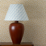 Table with decorative lamp against wallpaper in a lyrical wildflower design in cream with blue accents on a tan field. 