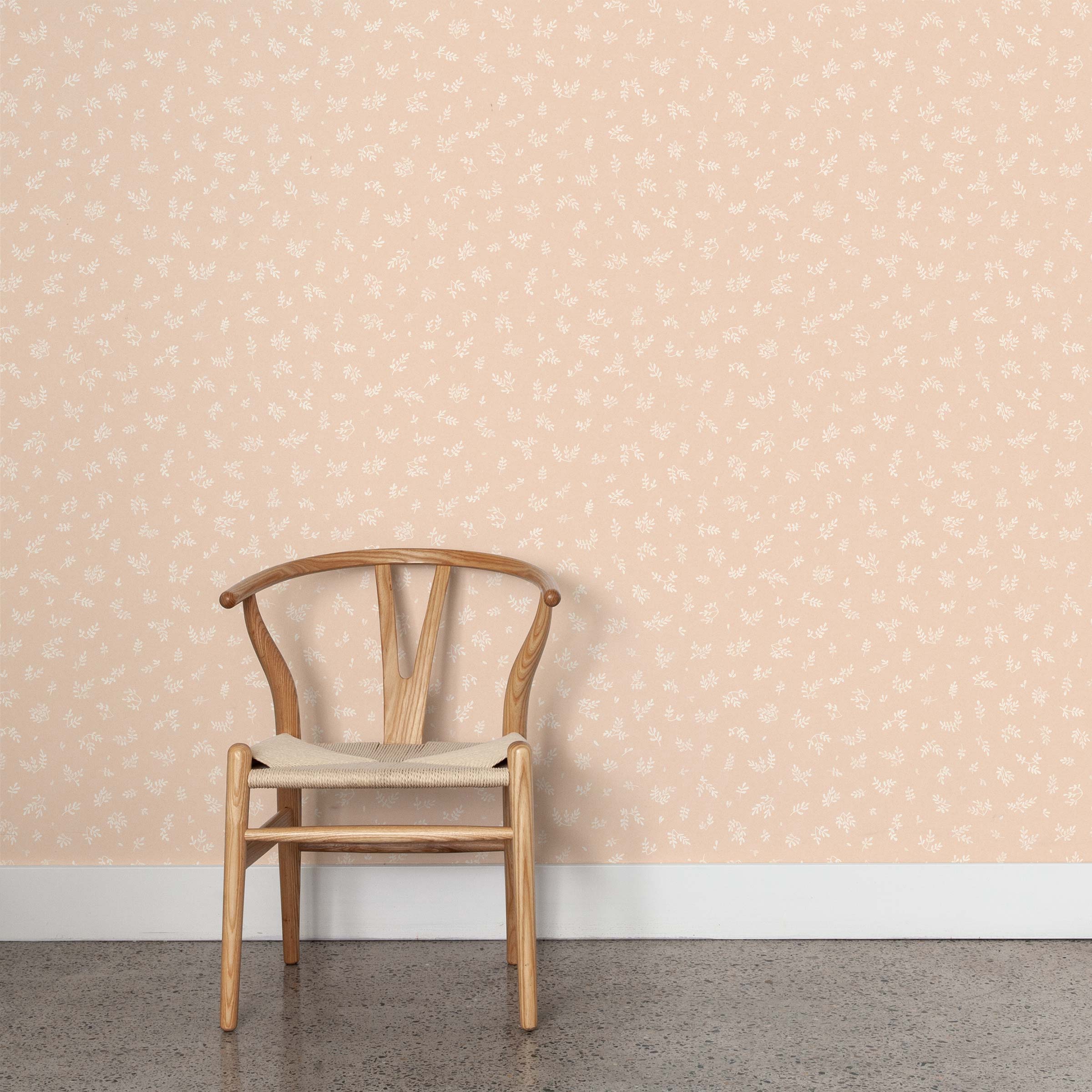 A wooden chair stands in front of a wall papered in a minimal repeating leaf print in cream on a light pink field.