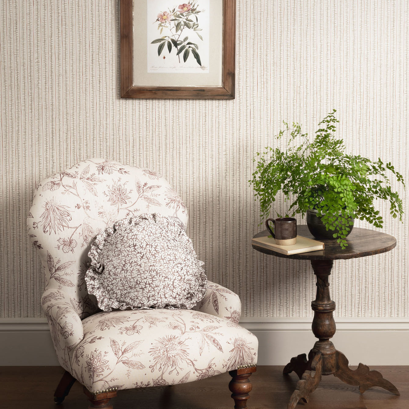 Decorative armchair with floral pattern, side table with plants, and framed artwork on striped wall.