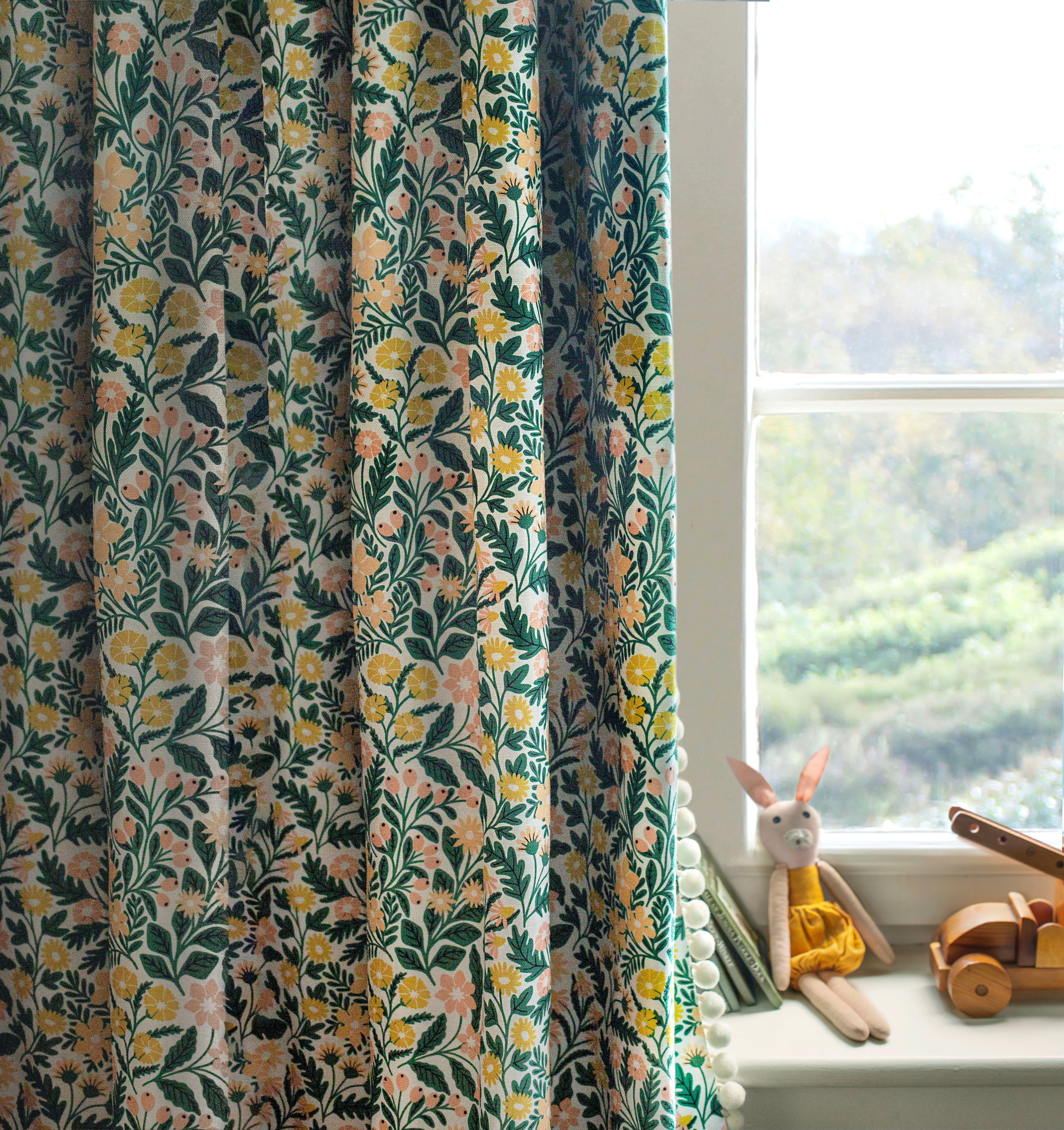 A children's room with a window and curtain in a small-scale floral print in green, yellow and coral on a white field.