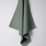 Draped woven outdoor fabric in a subtle stripe design in green and blue on a white wall. 