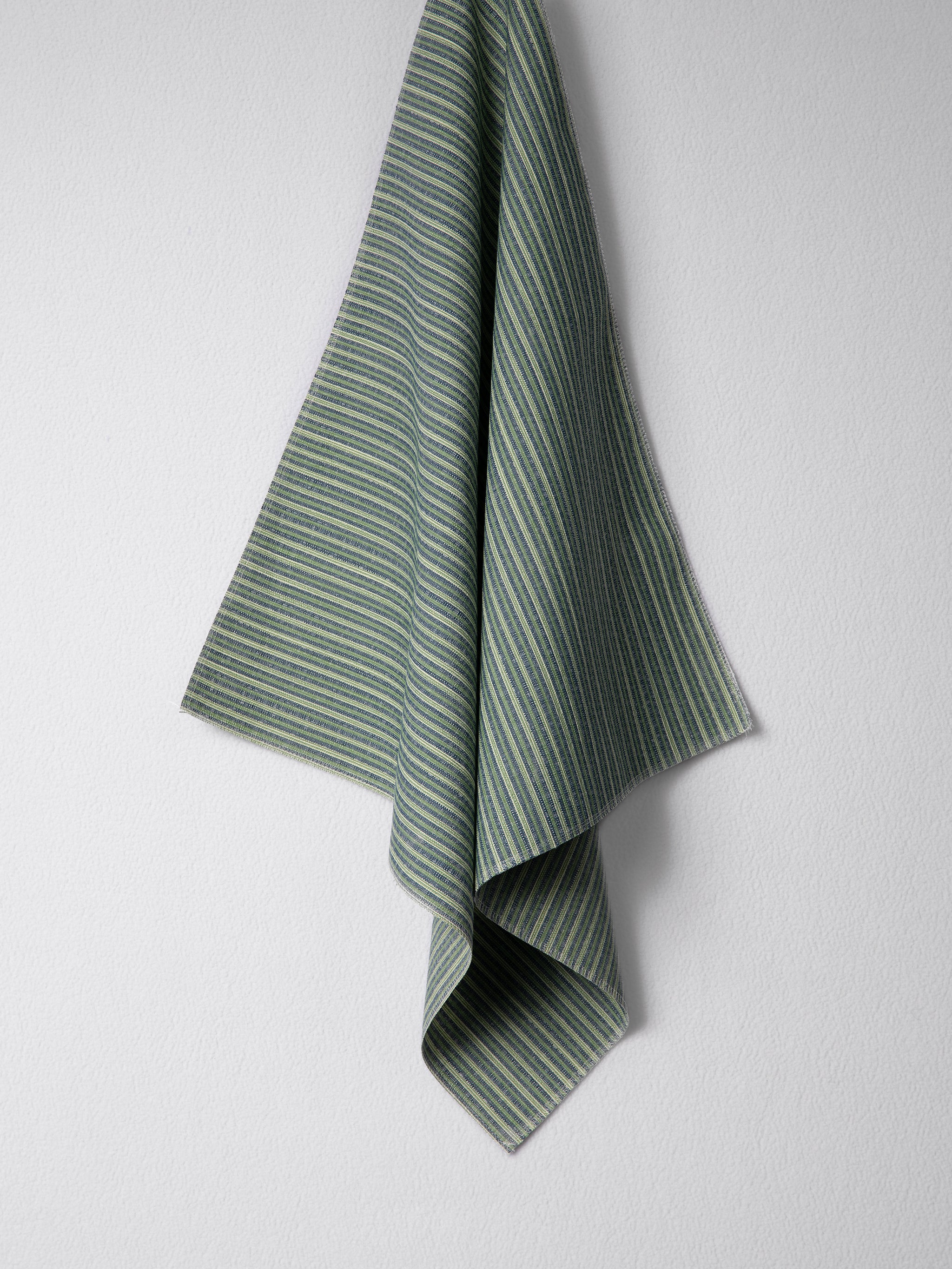 Draped woven outdoor fabric in a subtle stripe design in green and blue on a white wall. 