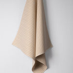 Draped woven outdoor fabric in a subtle stripe design in tan on a white wall. 