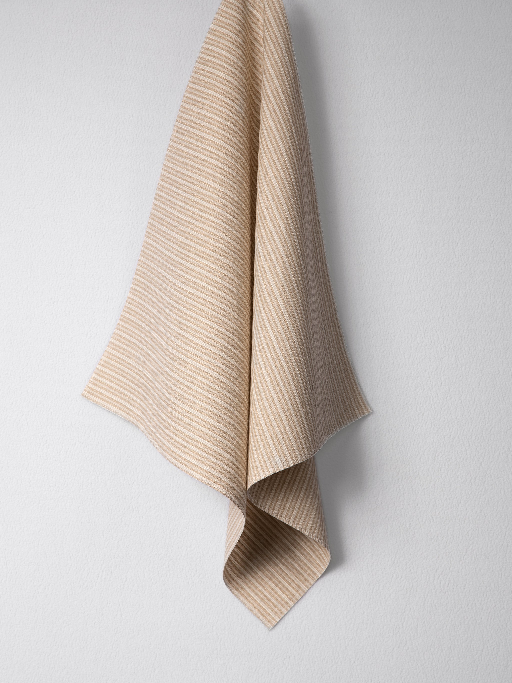 Draped woven outdoor fabric in a subtle stripe design in tan on a white wall. 