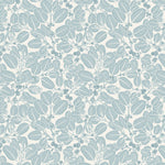 Two wooden chairs stand in front of a wall papered in a dense leaf and stem print in blue-gray and white.