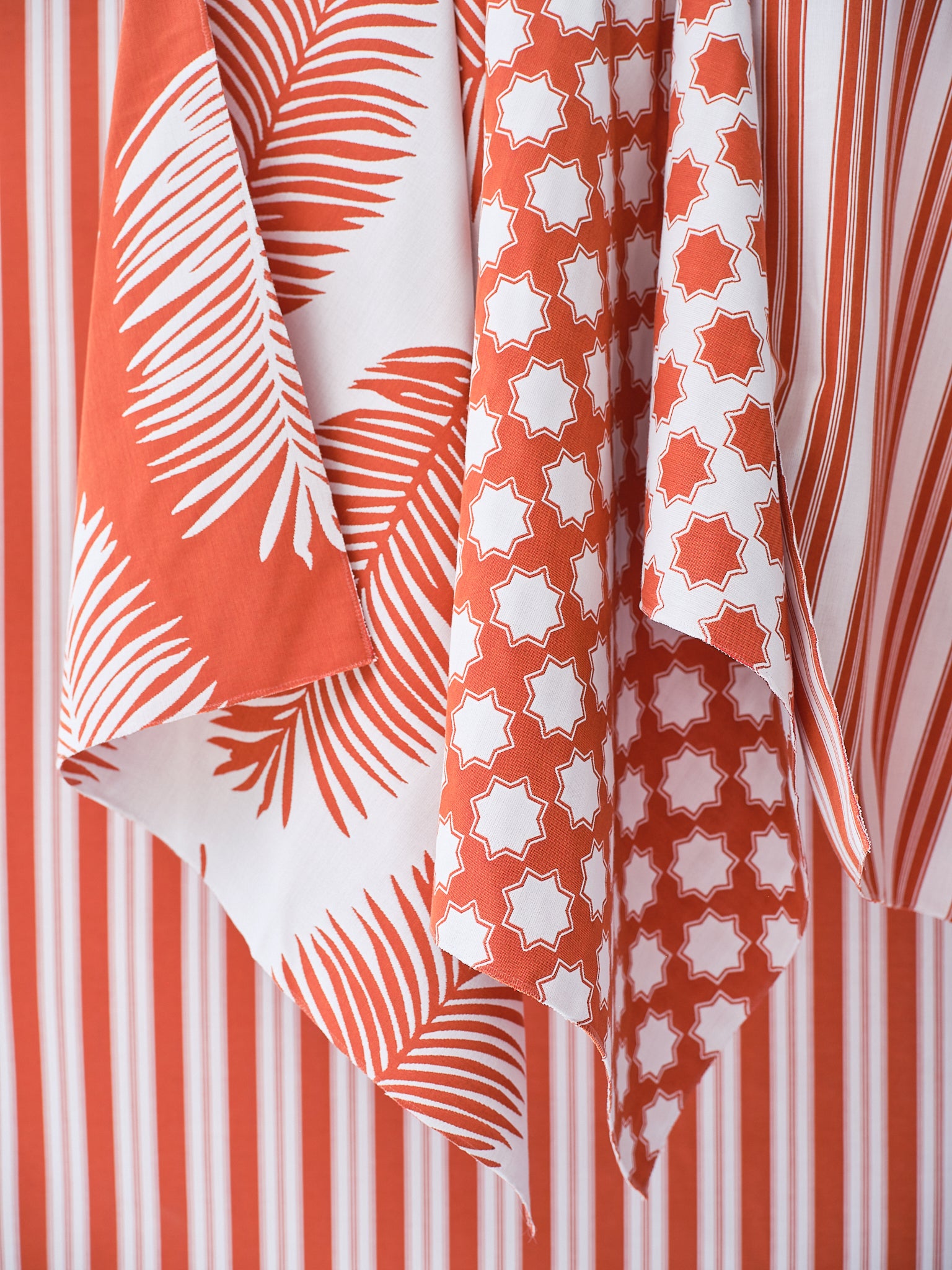 An array of bright orange and white performance fabrics in a palm print, moroccan star and simple stripe.