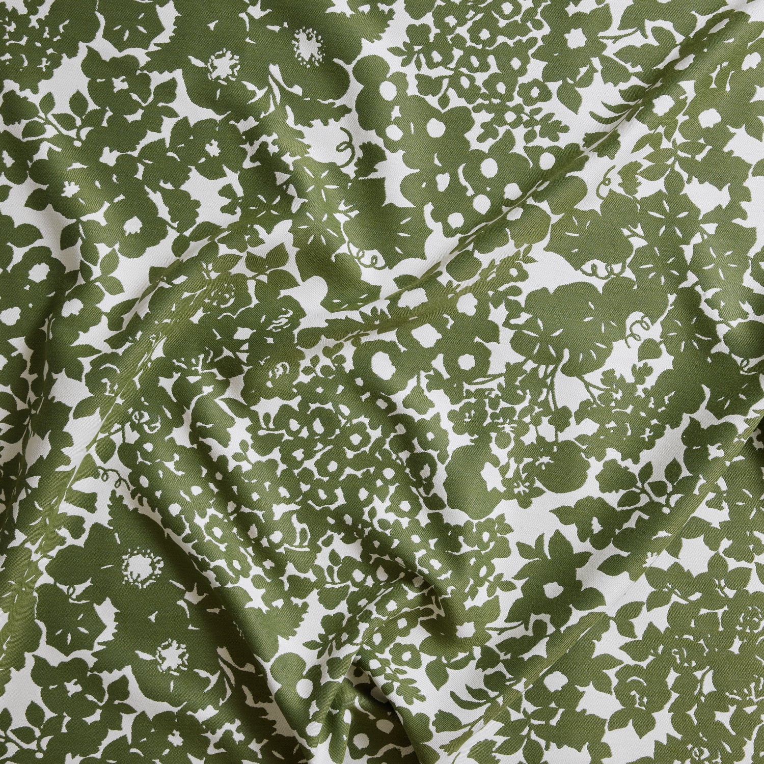 Close up of gently draped woven Indoor-Outdoor fabric with flower and leaf silhouette pattern in green on white background