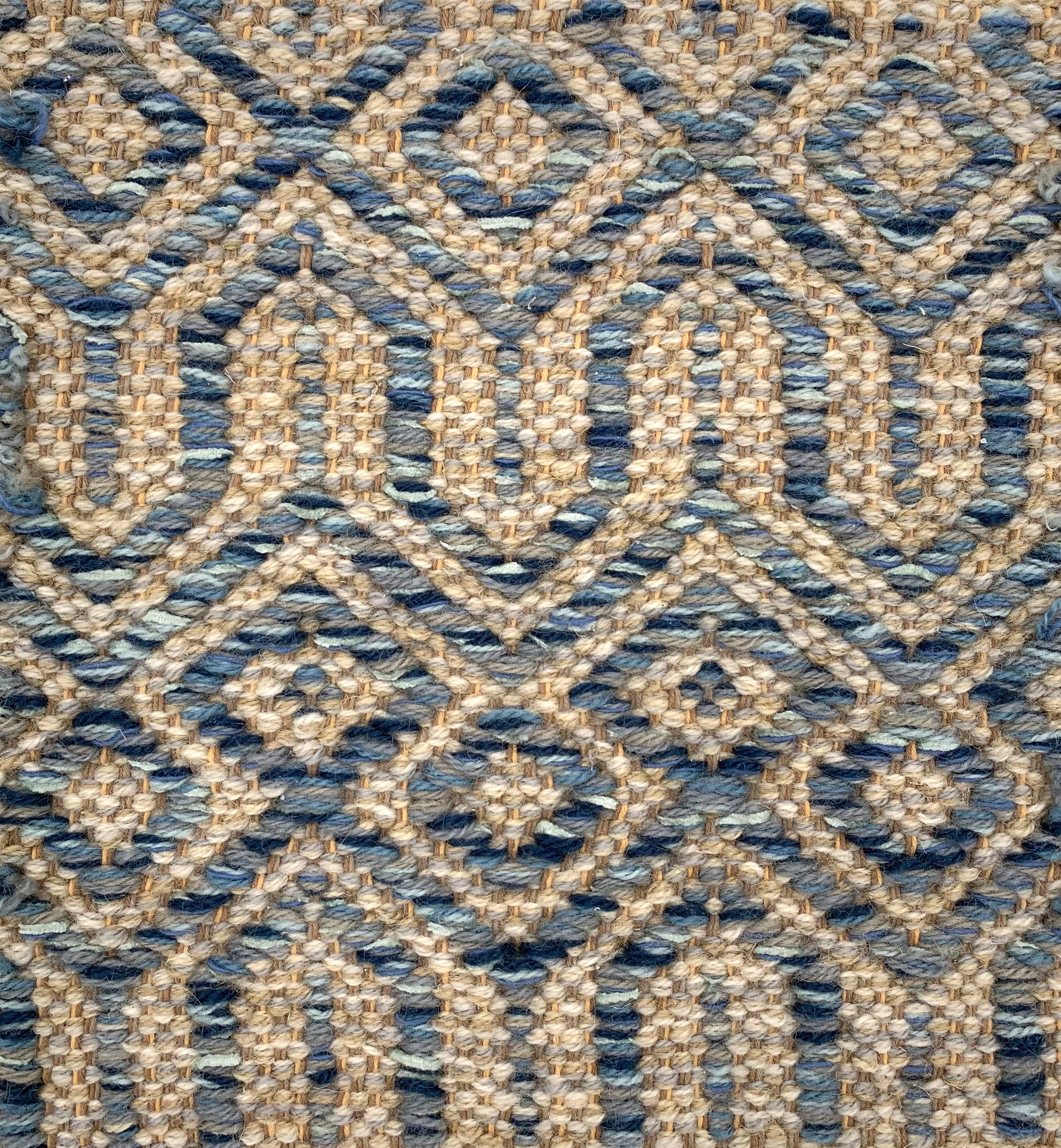 Handwoven carpet in a complex geometric lattice design in shades of blue on a beige field. 
