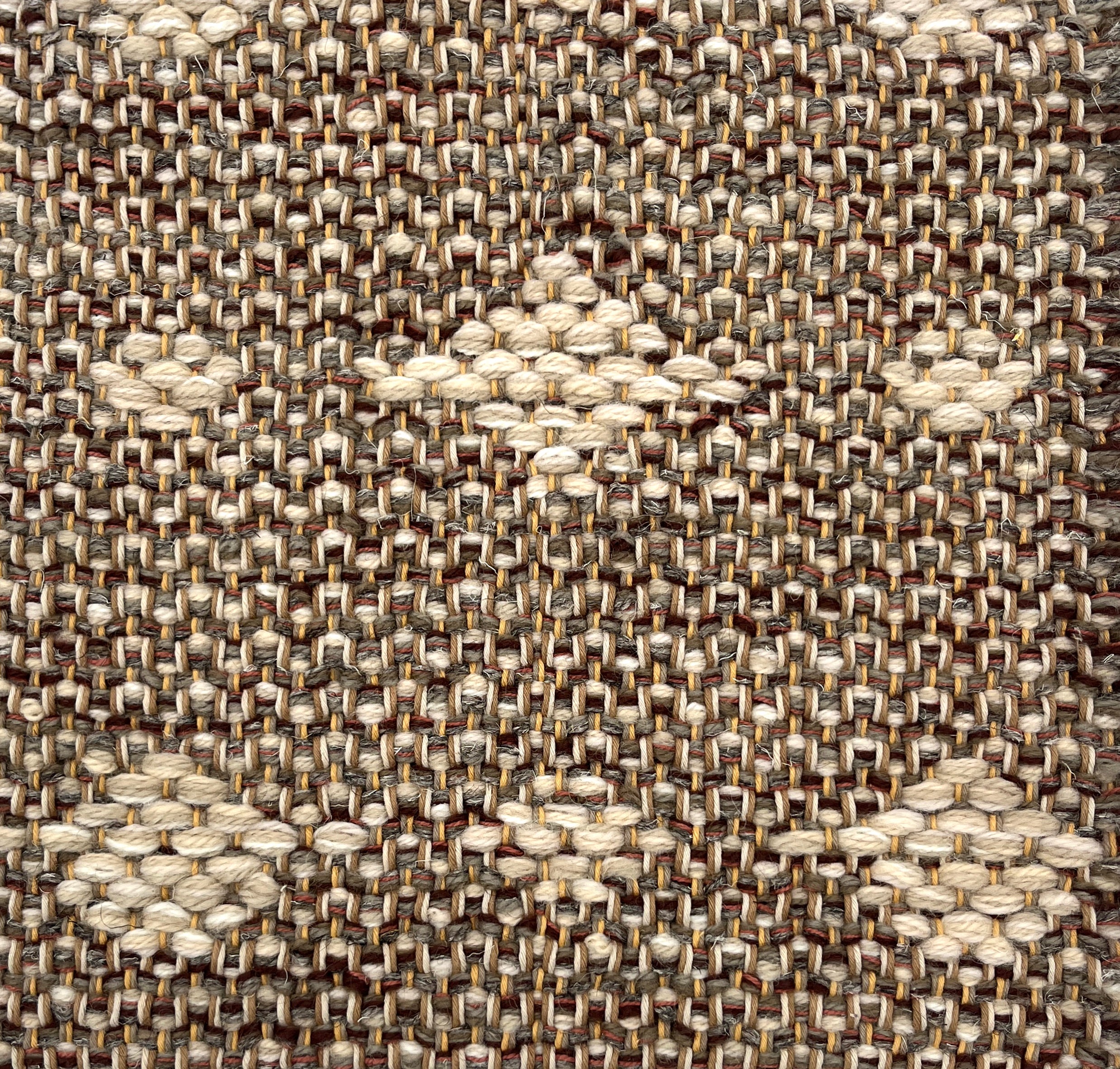 Close-up of a woven rug  with a diamond pattern in shades of cream on a brown field.