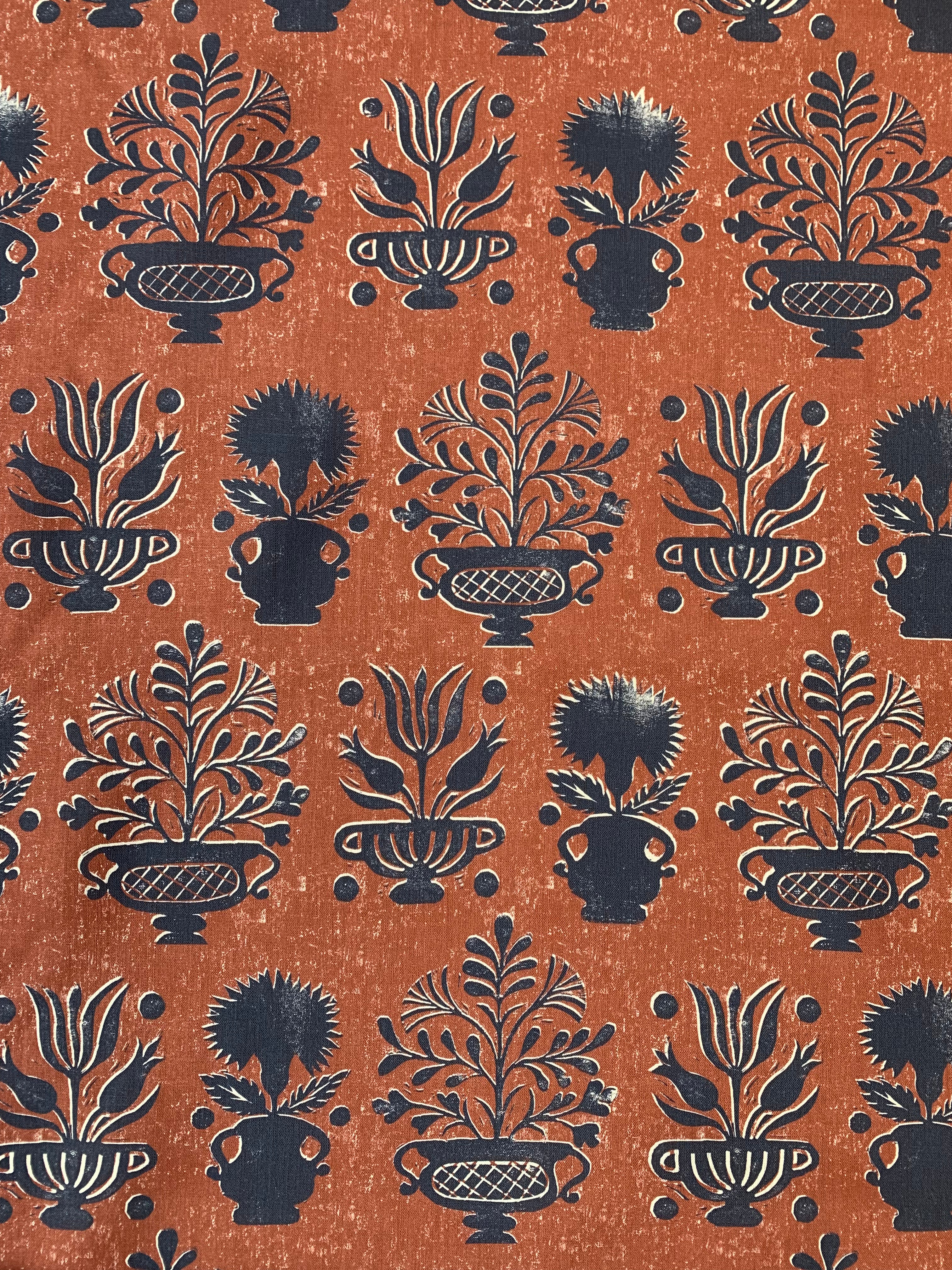 Detail of fabric in a repeating vase and plant print in navy on a mottled rust field.