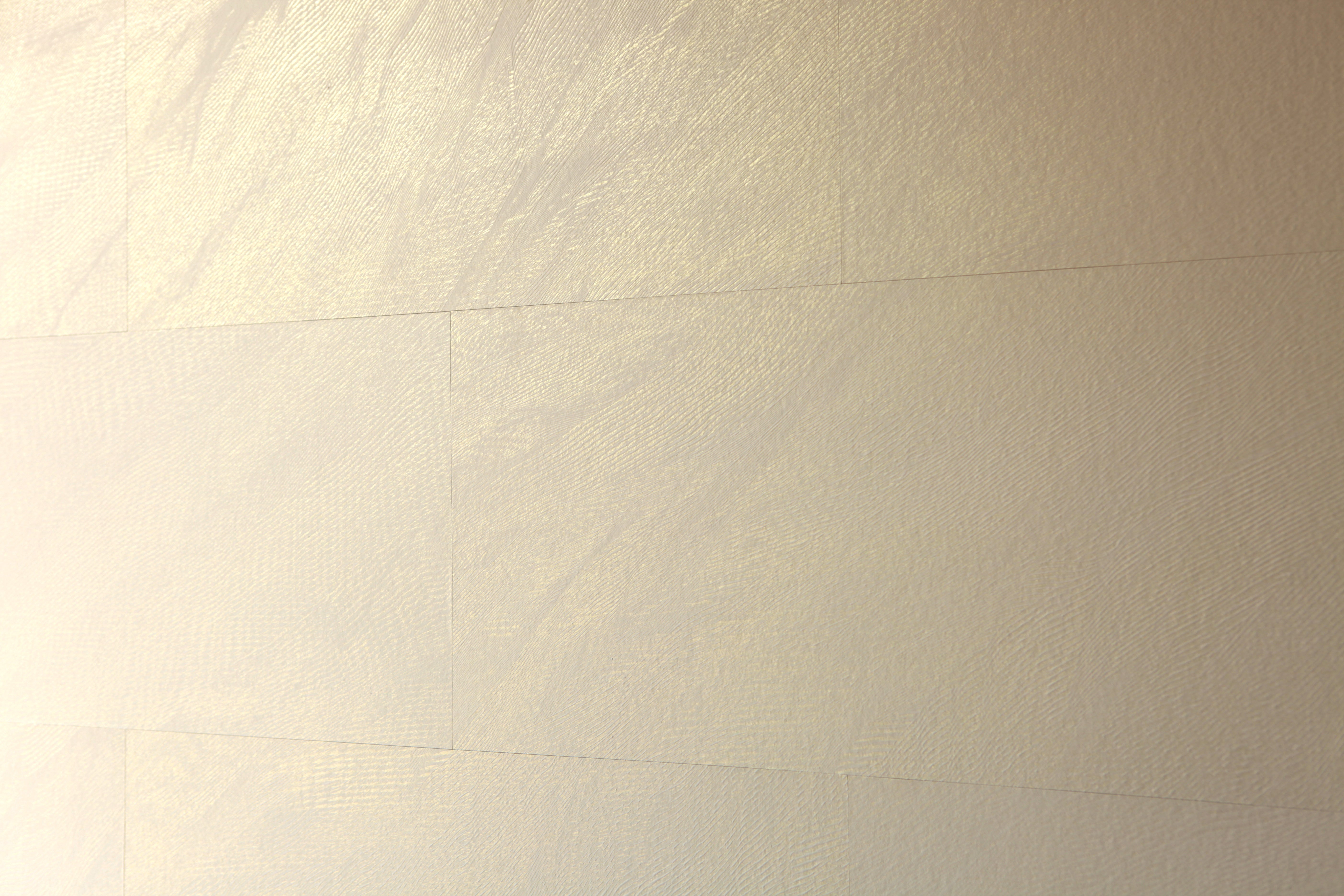 A wall papered in tiles of textured wallpaper in metallic gold and cream.