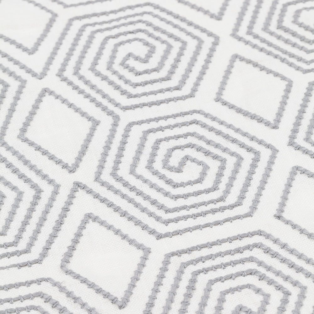 Detail of an embroidered fabric with a geometric spiral design in grey on a white field.
