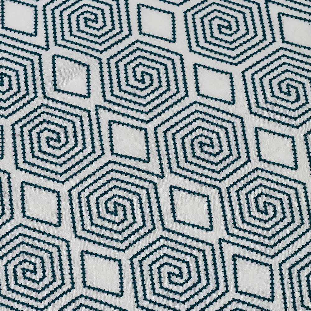 Detail of an embroidered fabric in a geometric spiral design in navy on a cream field. 