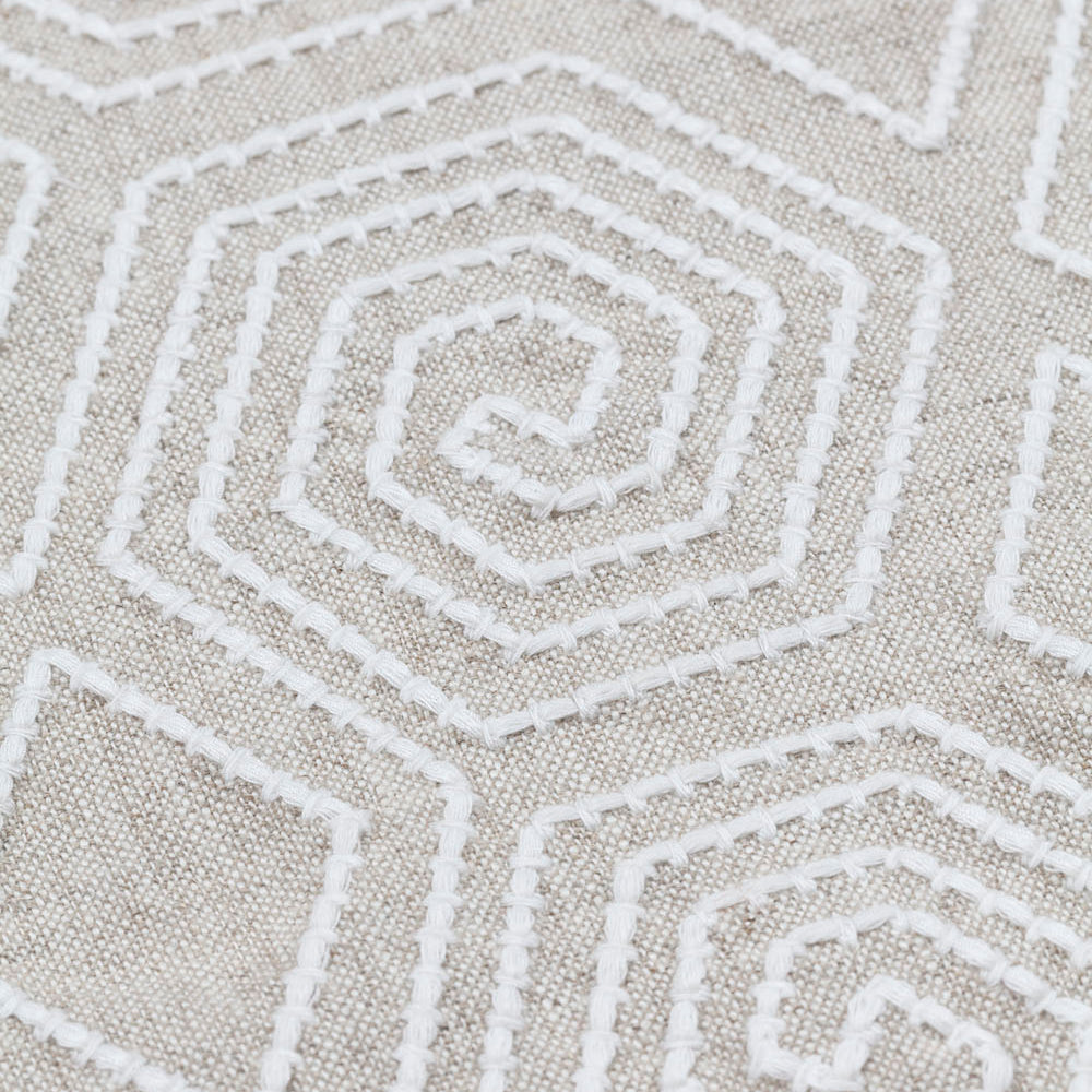 Detail of fabric with a playful embroidered geometric grid print in white on a cream field.