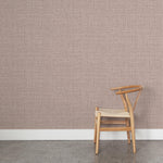 A wooden chair stands in front of a wall papered in a textured tweed pattern in shades of purple.