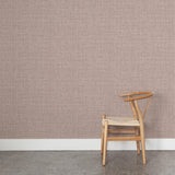 A wooden chair stands in front of a wall papered in a textured tweed pattern in shades of purple.