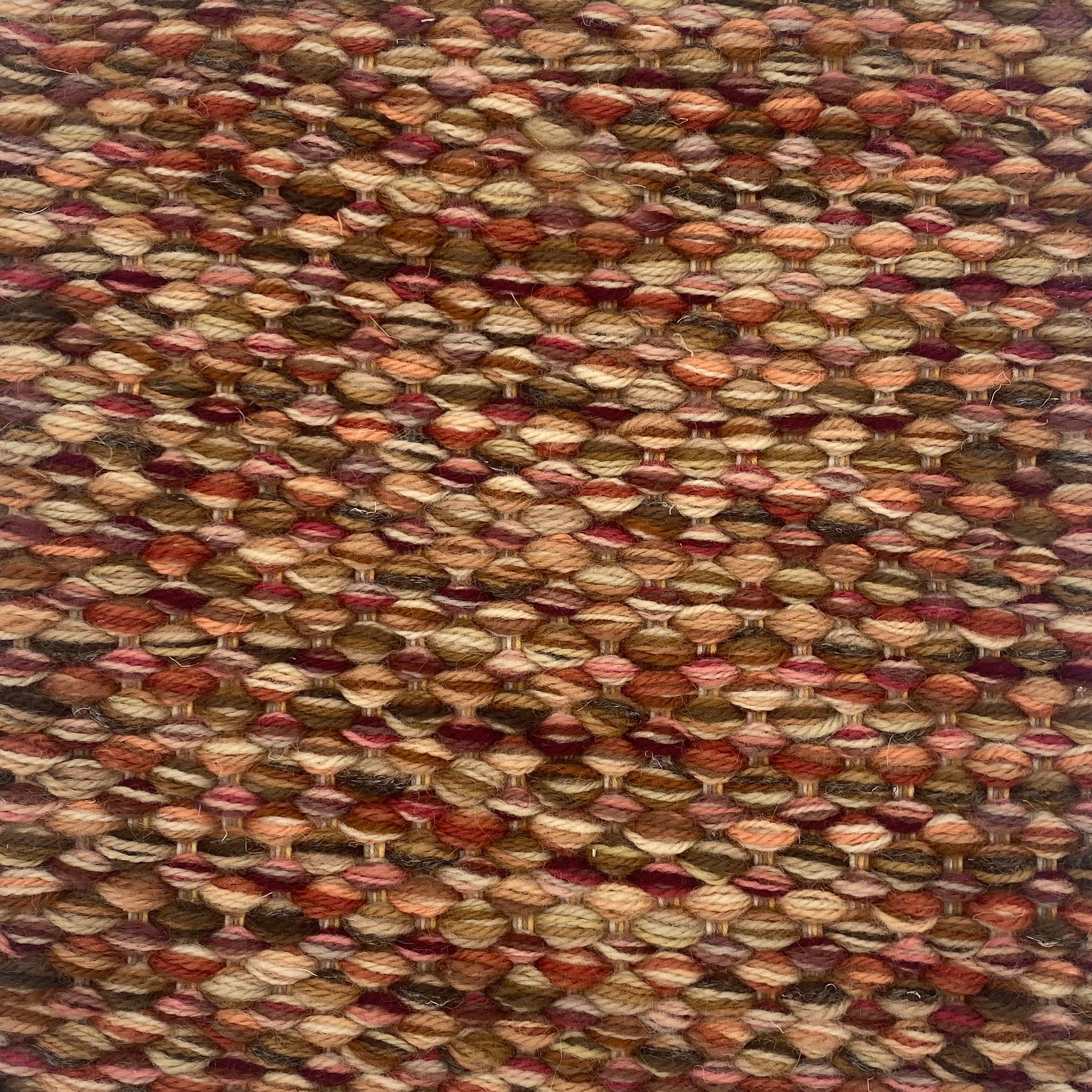 Textured handwoven carpet with a mix of red, rust, and brown.