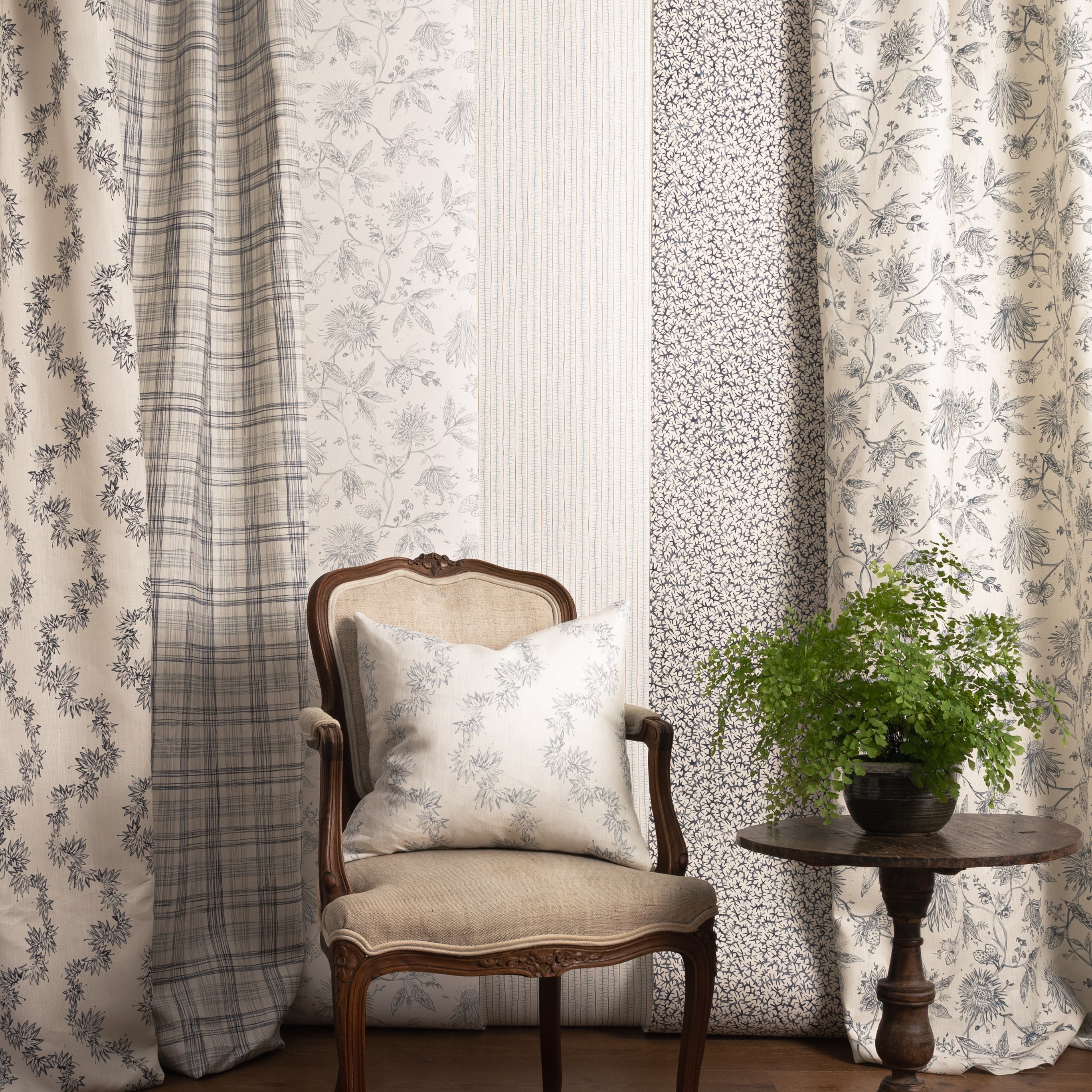 Chair with a pillow in front of panels of fabric and wallpapers in various patterns in blue colors.