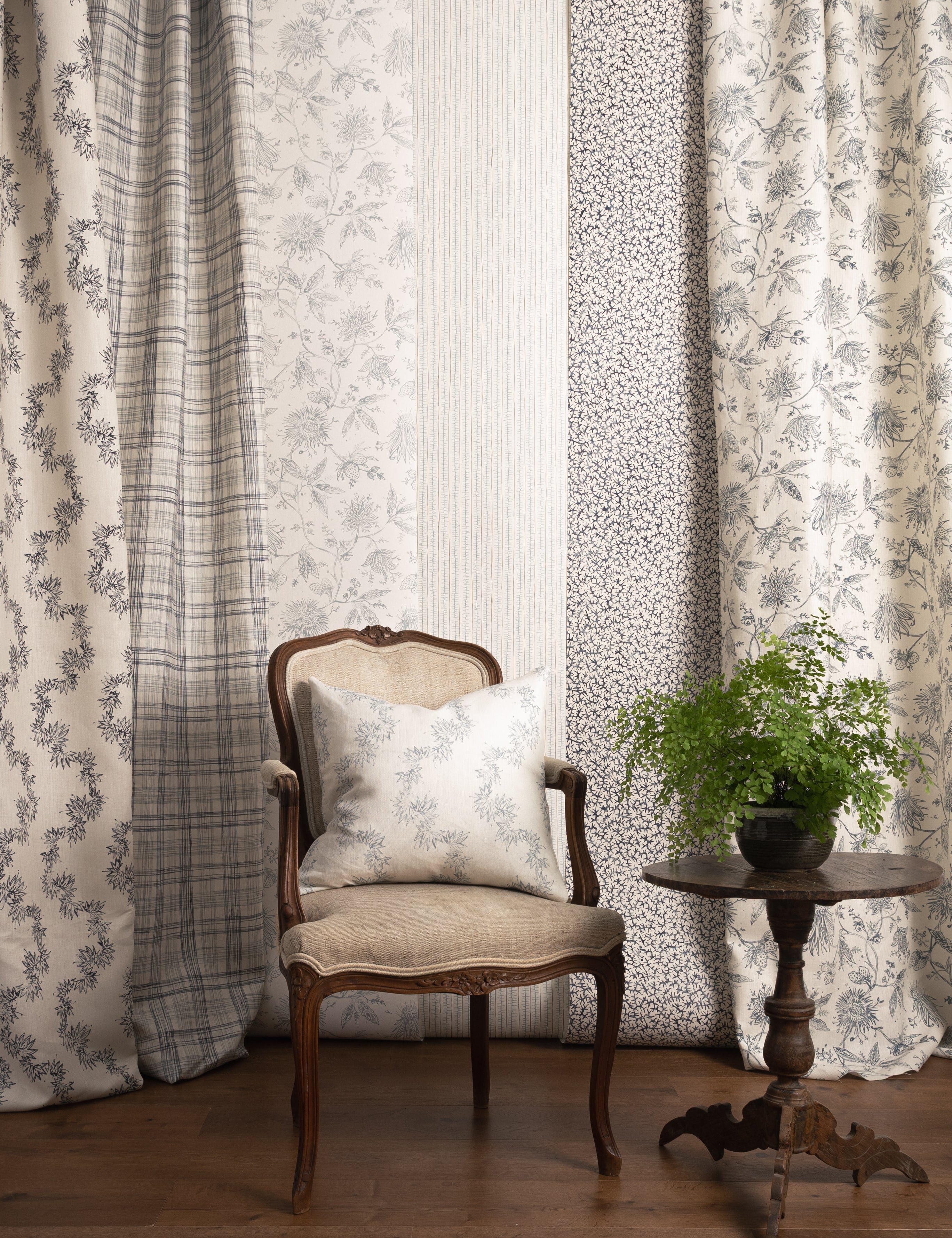 Chair with a pillow in front of panels of fabric and wallpapers in various patterns in blue colors.